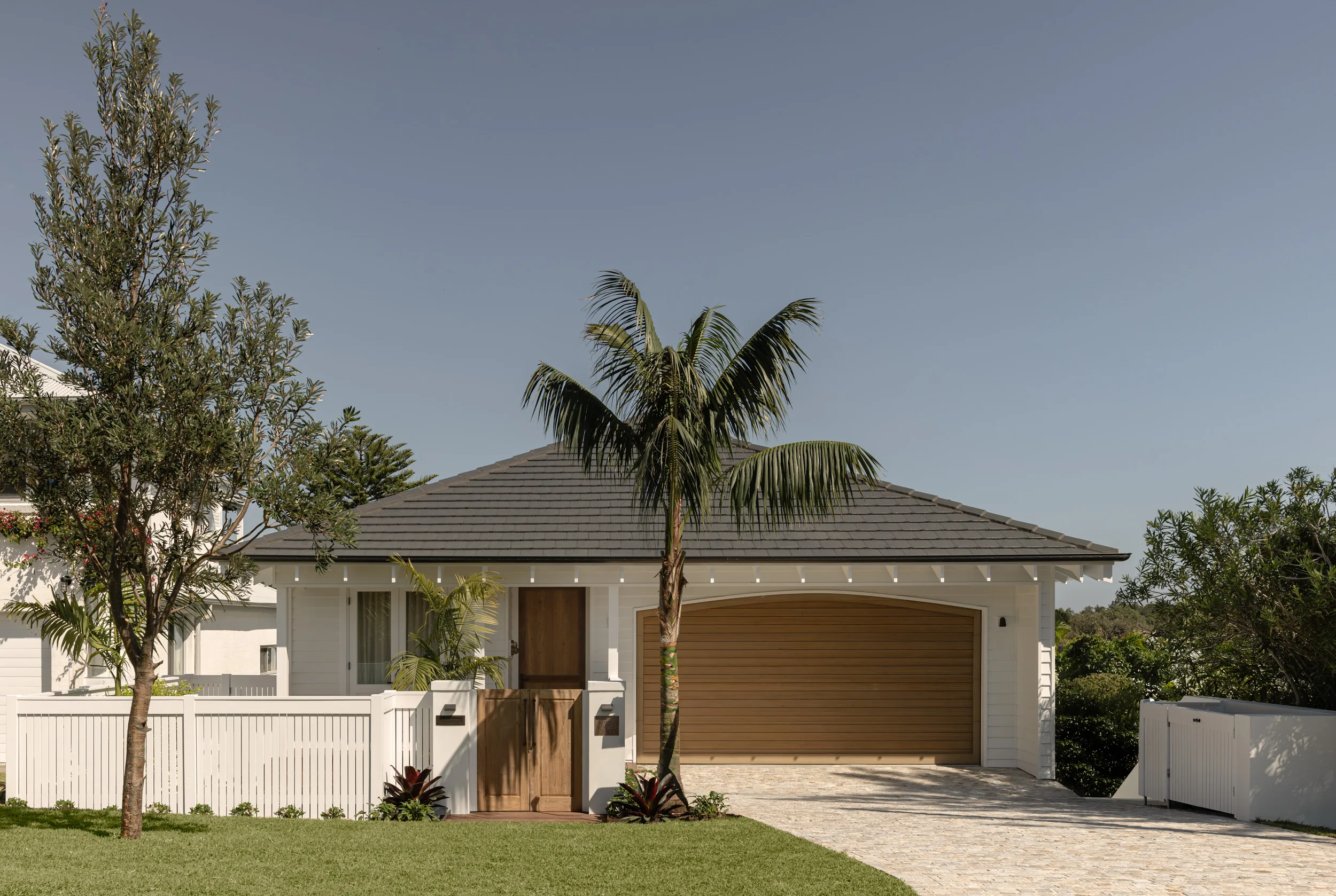 The front facade of a Bahamian inspired country house with a palm tree and a black roof