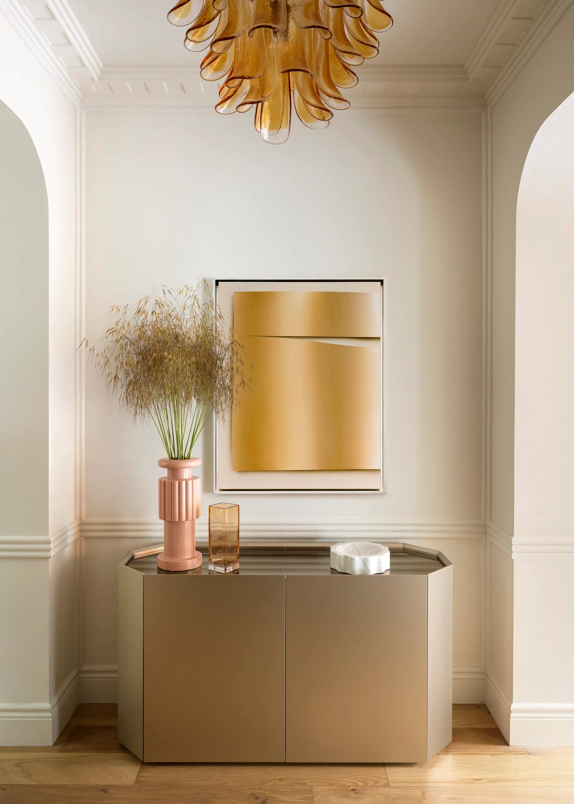A metal buffet in a large hallway beneath an abstract glass chandelier
