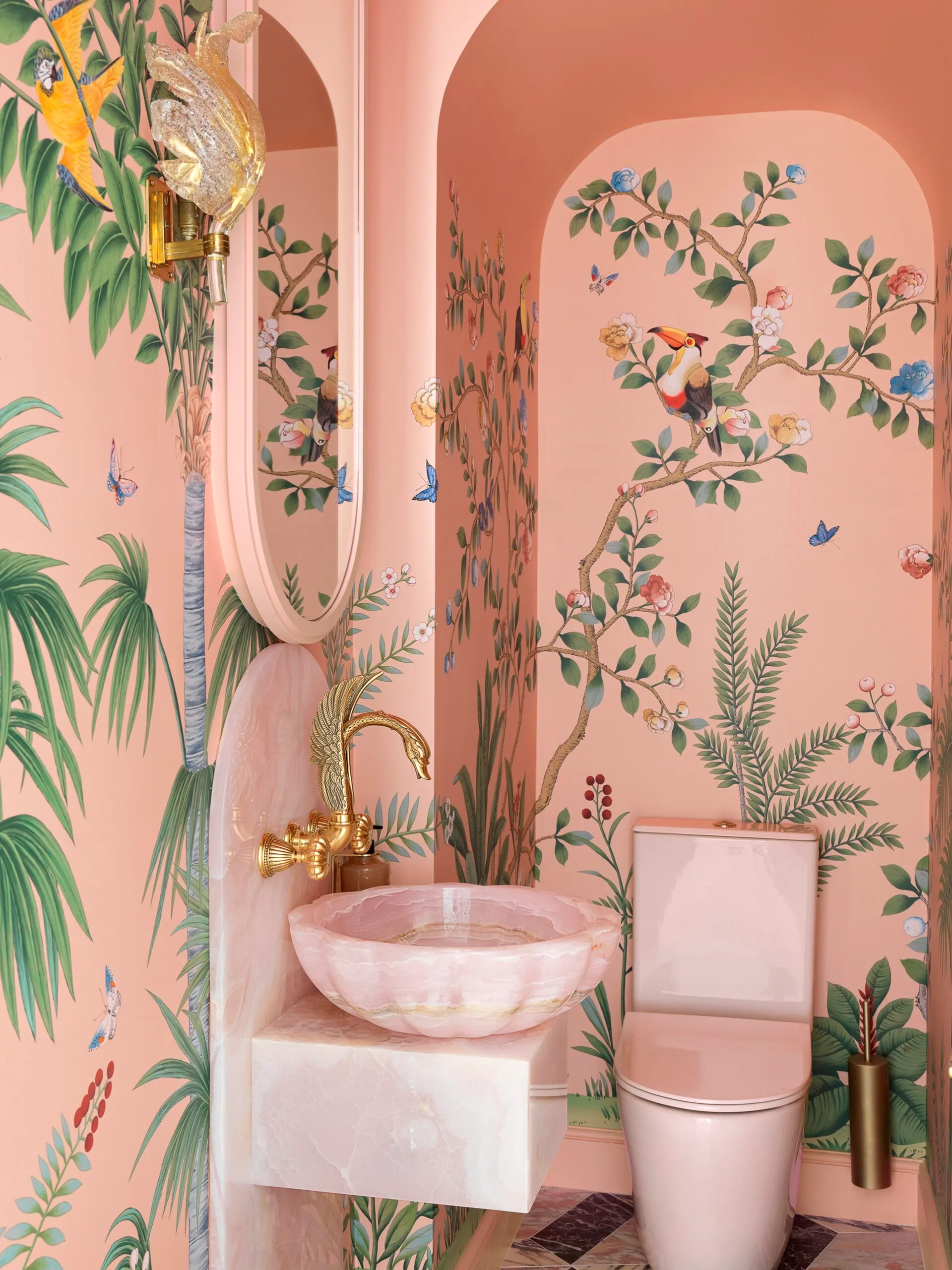 A pink powder room with whimsical tropical wallpaper and a statement pink sink and bird shaped faucet