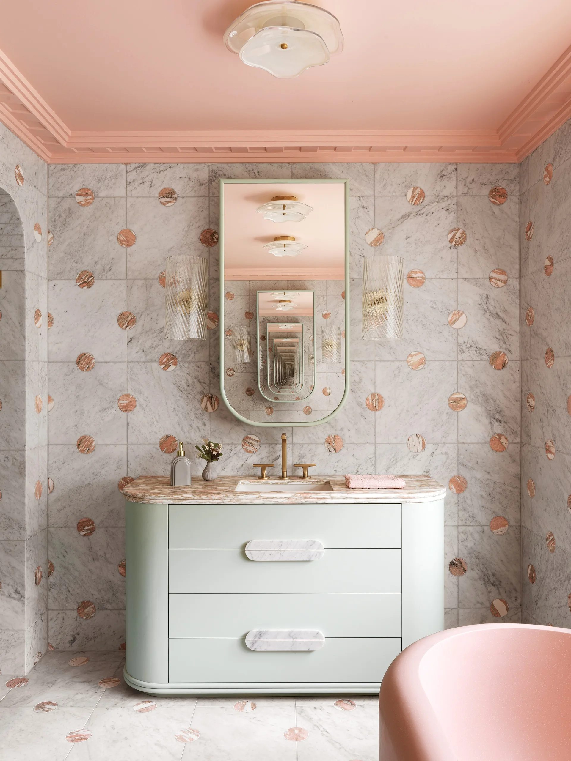 A marble and pink bathroom with a mint green vanity
