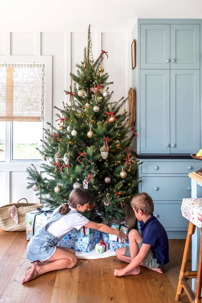 A Christmas tree is decorated with festive baubles and bows, while kids explore the presents underneath.