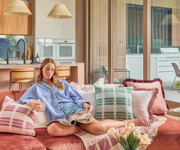 A person reclined on a pink sofa decorated with pillows and a throw blanket