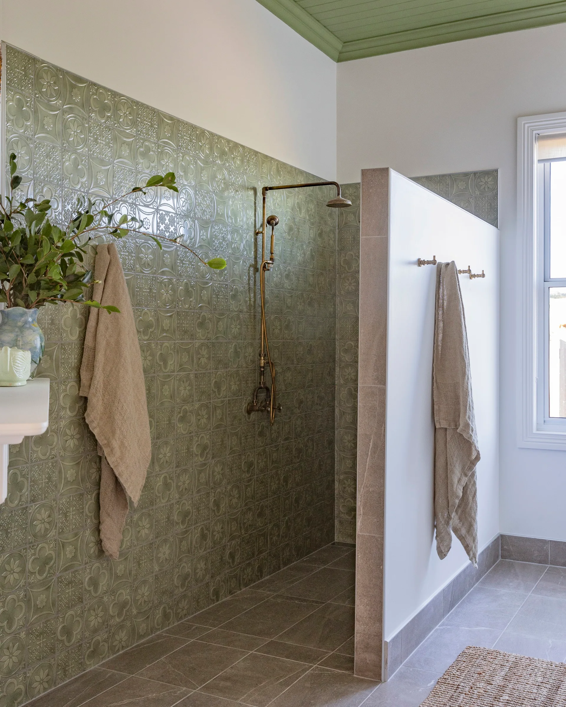 A walk-in shower with green patterned tiles and a painted green ceiling