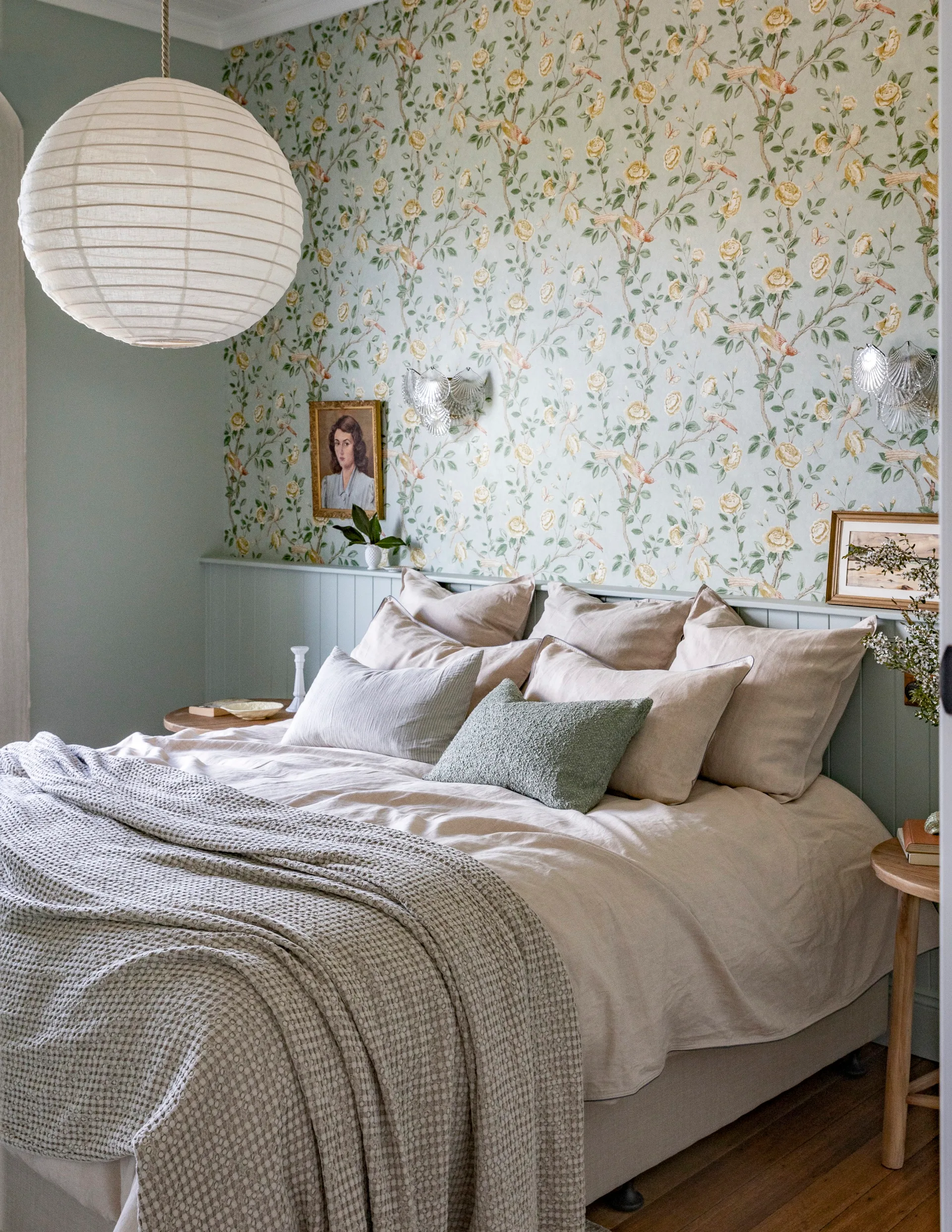 A bedroom with pale blue patterned wallpaper, decorative panelling and a paper light