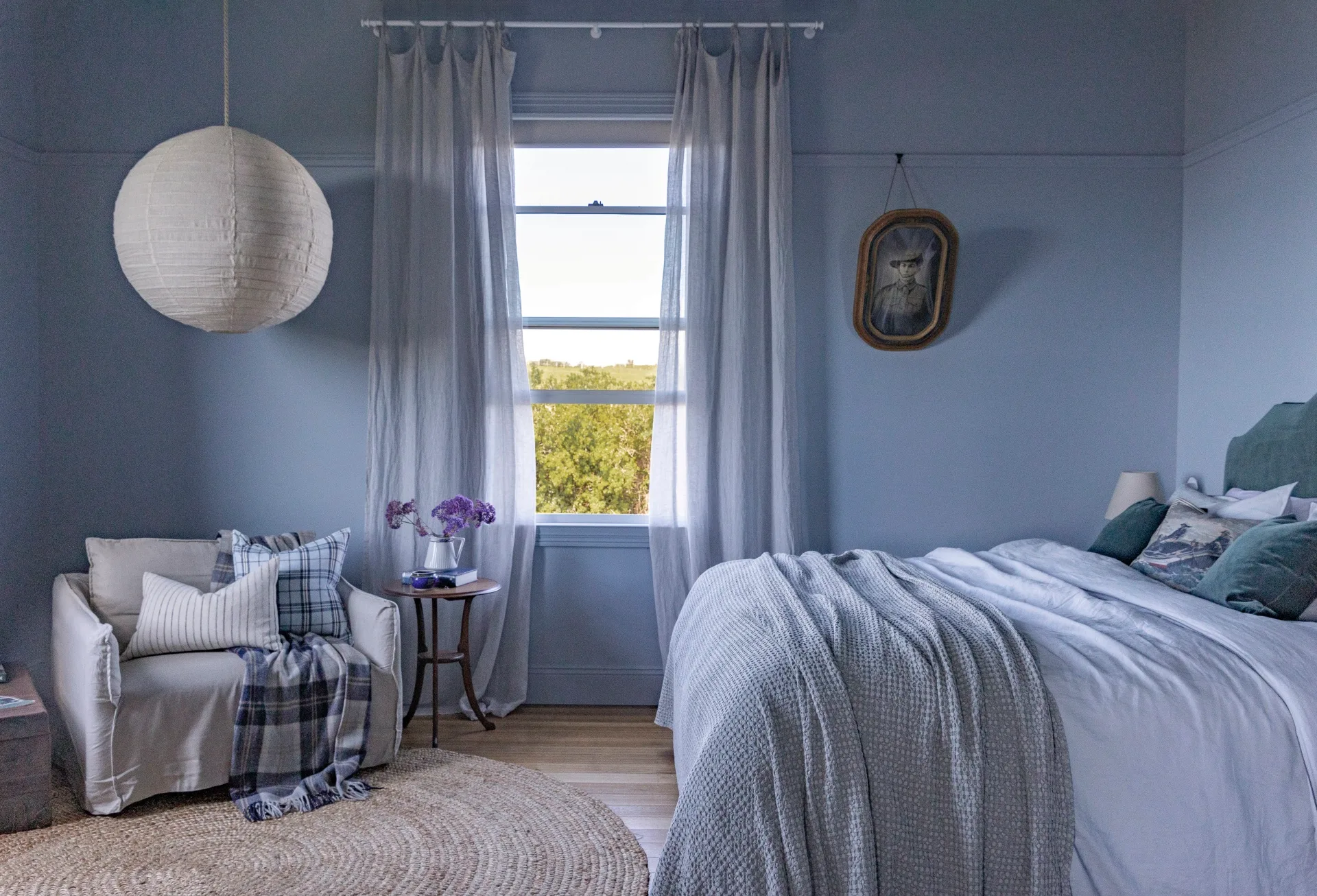 A bedroom with powder blue walls, a large paper light and blue bedding