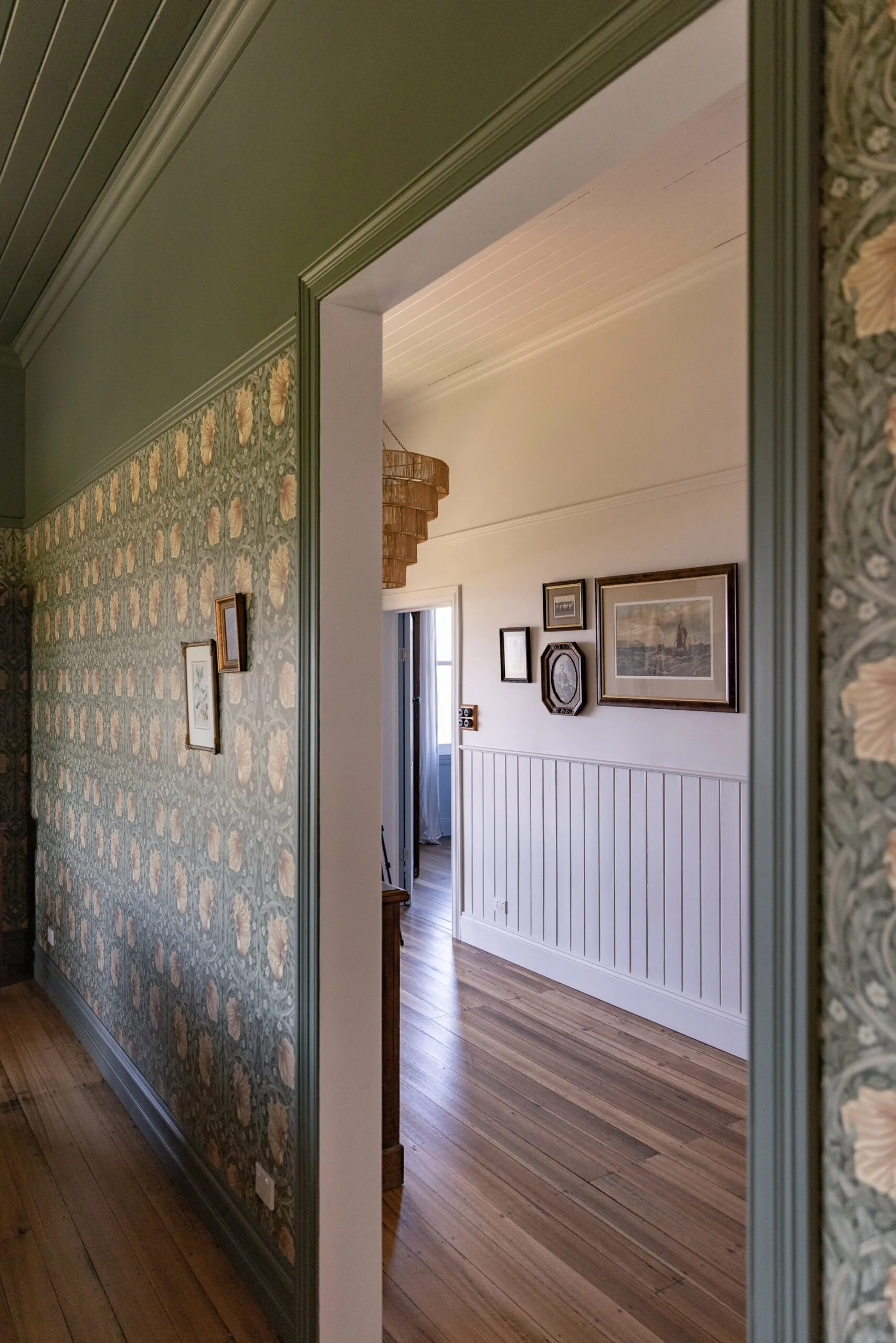 A glimpse into a hallway with wooden floorboards, white decorative wall panelling and historic paintings on the wall