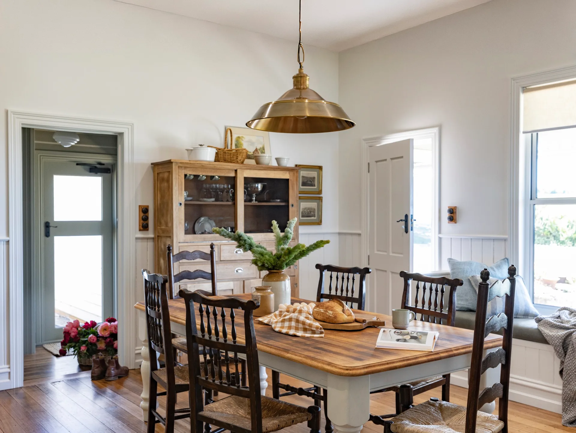 A dining room with a large, wooden table, a cosy window seat and a large, industrial pendant light