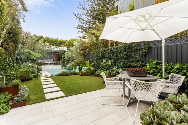 An alfresco dining area overlooking a swimming pool and lush garden