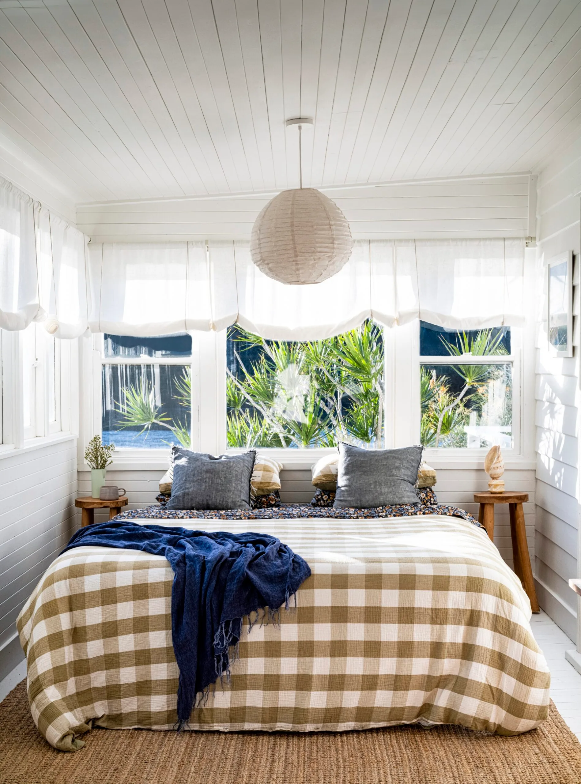 A cottage bedroom with white walls, sheer London blinds and a paper pendant light.