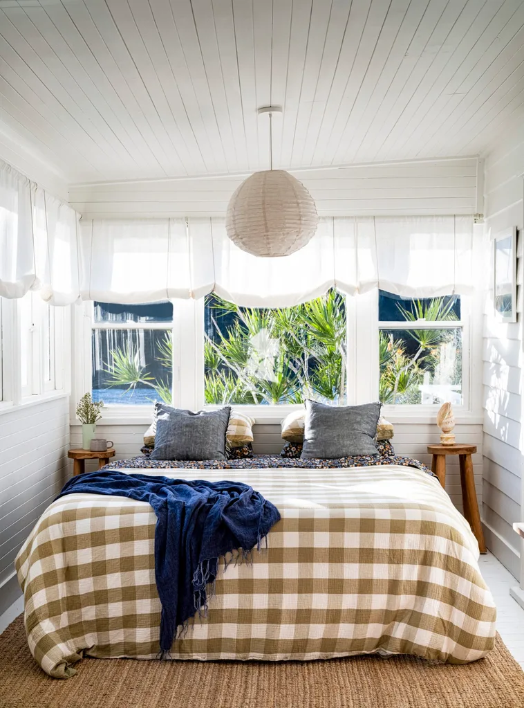 A cottage bedroom with white walls, sheer London blinds and a paper pendant light.