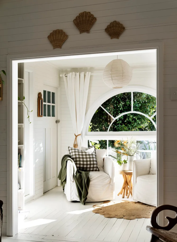 A sunroom with a large arched window looks out onto a leafy vista.