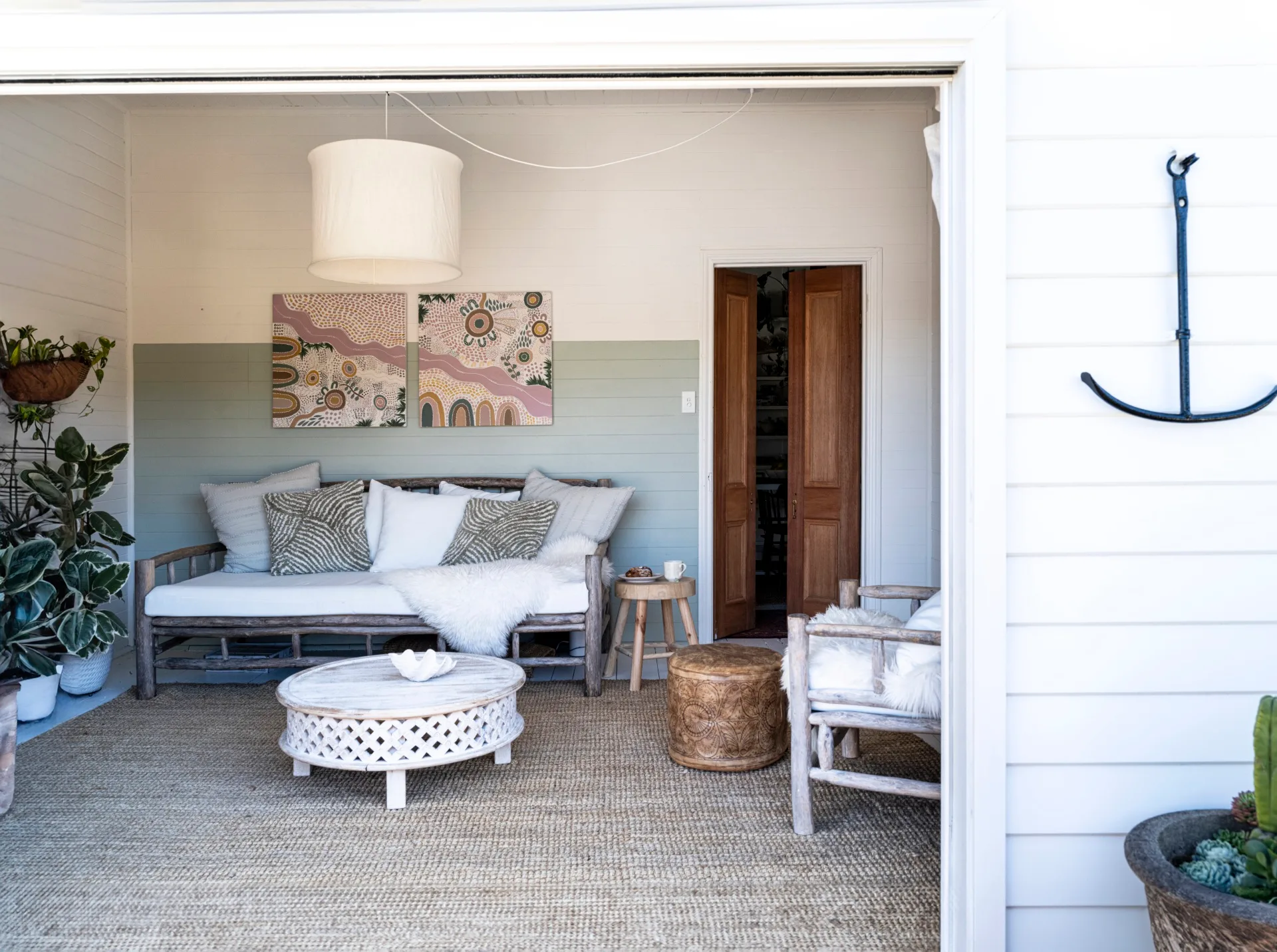 A coastal living room with white walls and rustic furniture. An aboriginal artwork hangs on the wall.