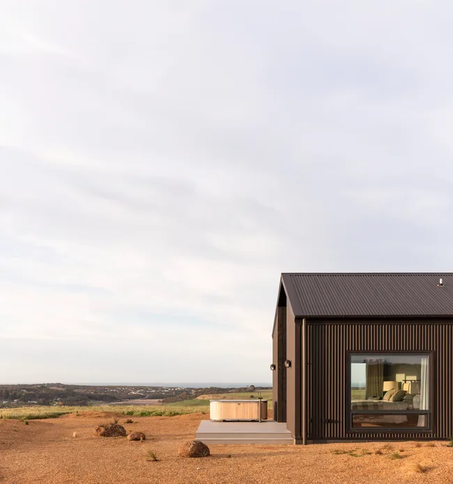 The exterior of a country home made from corrugated black cladding with a bath on the outdoor deck.