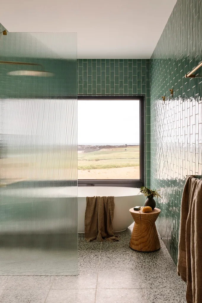 A bathroom with glazed green tiles, a white bath and a view out to the rolling hills beyond.