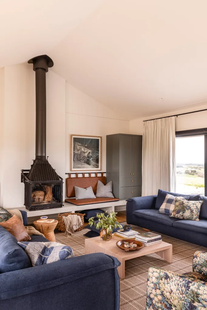 A cosy, country style living room with large, dark blue sofas, a dramatic black fireplace and a leather built-in bench seat.