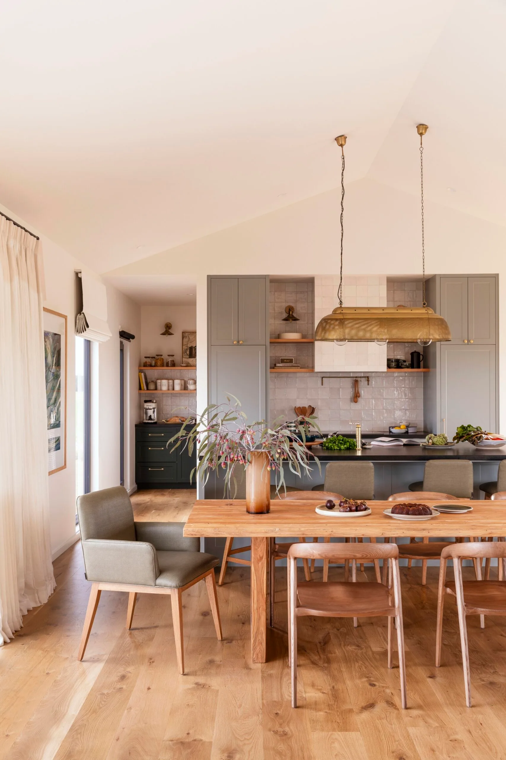 A bright, country-style kitchen and dining room with wooden floor and sage-coloured cabinetry.