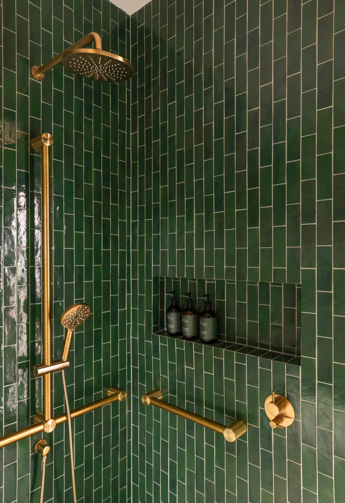 A shower area with glossy green floor-to-ceiling tiles, gold hardware and a niche.