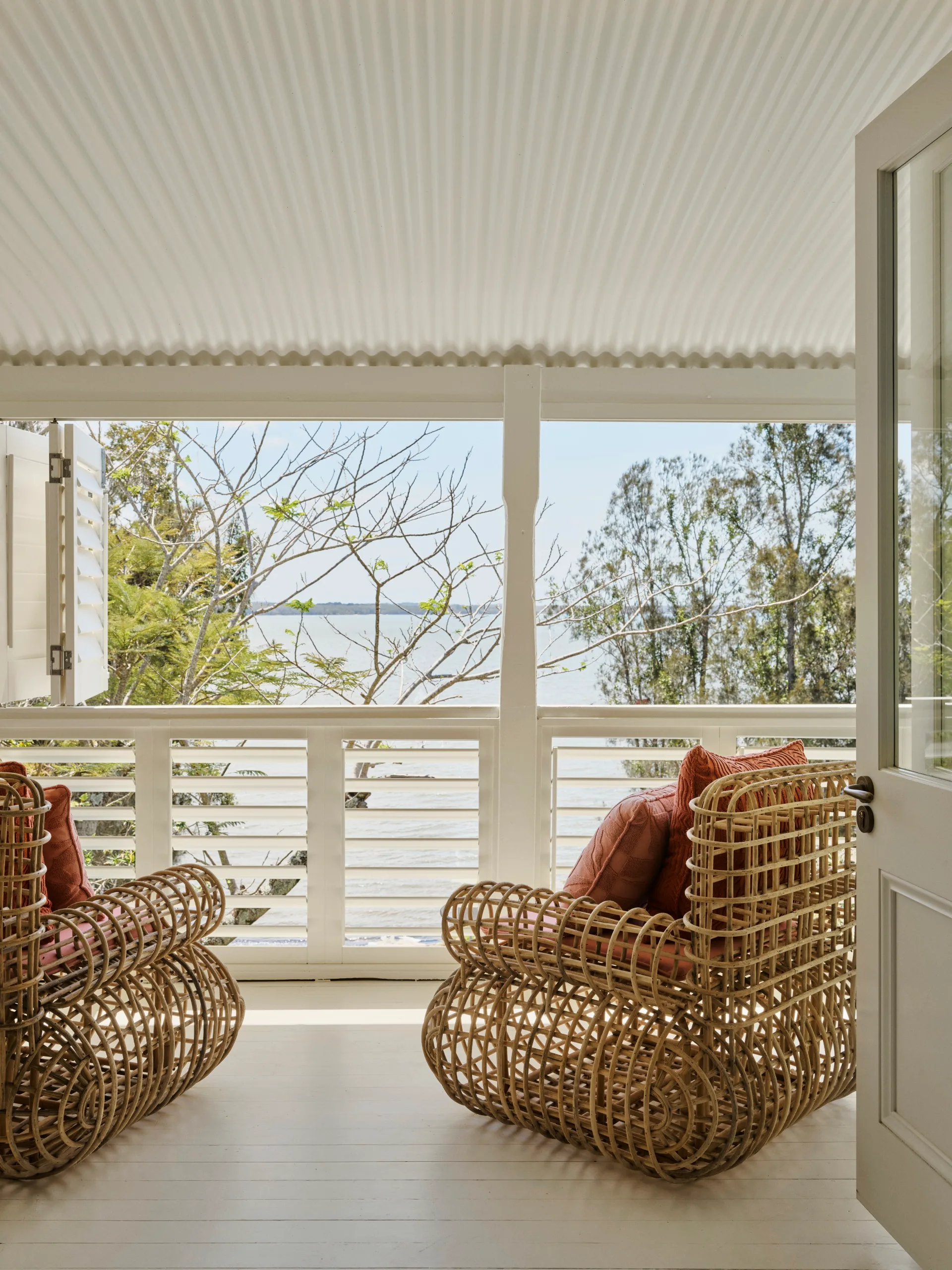 A white porch with two rattan chairs overlooking the water
