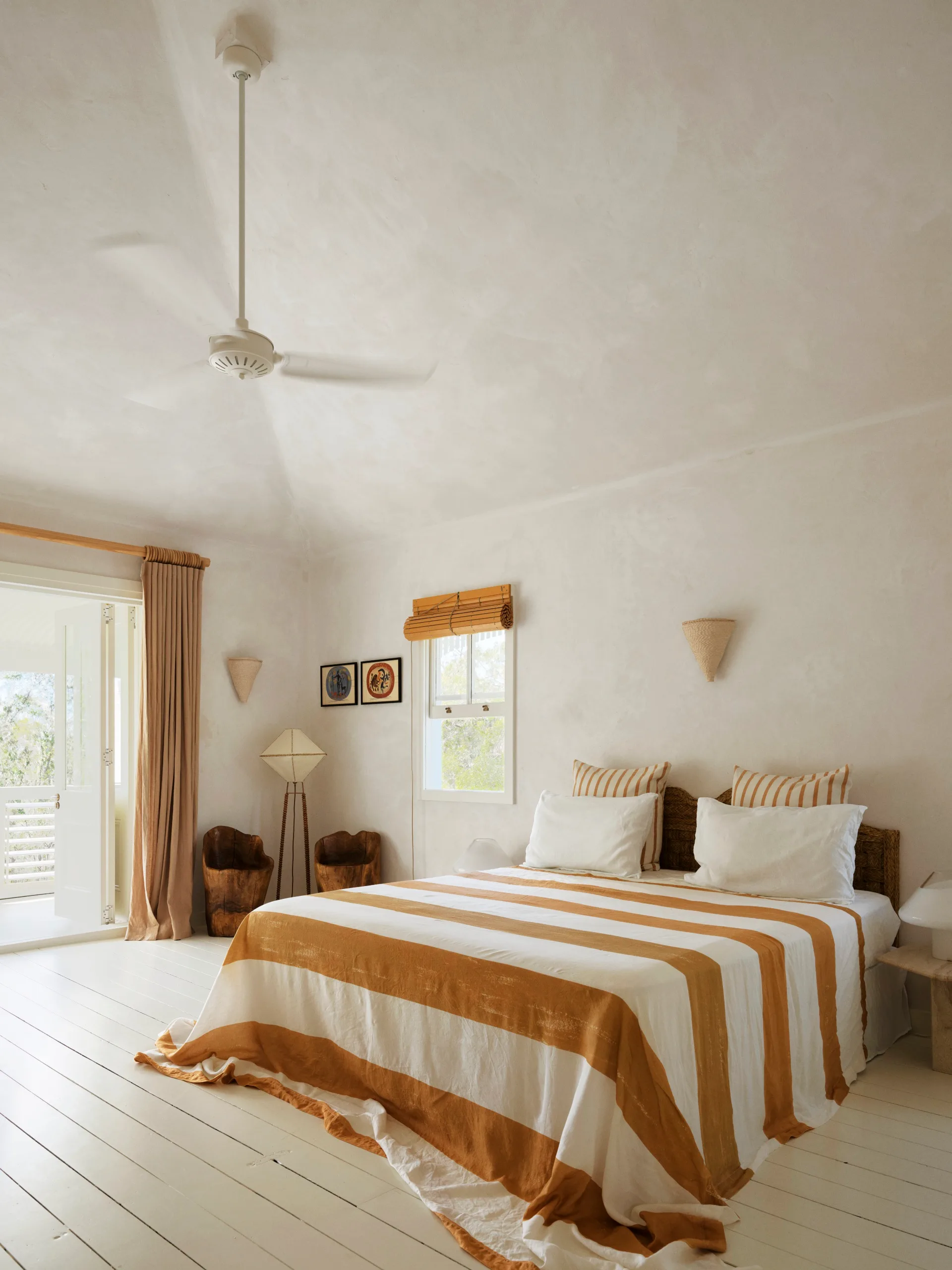 A beige bedroom with high ceilings and a bed draped in striped linen