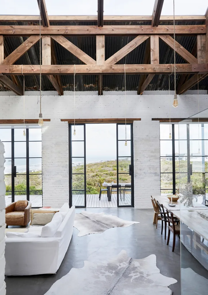 A large, barn-style living room with a high ceiling and large doors looking out to a coastal view