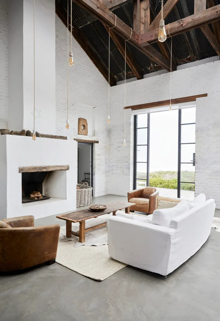 In a barn-style living room, rustic furniture is oriented around a large fireplace.
