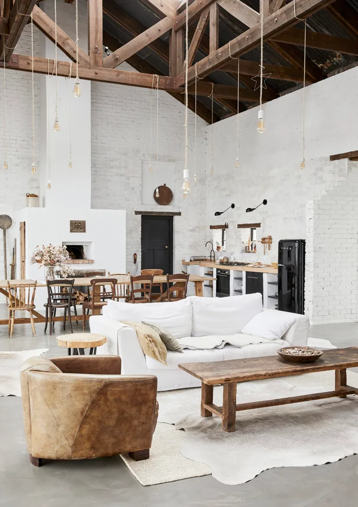 A barn-style living room with exposed beams and rustic wooden furniture. The exposed brick walls are painted white.