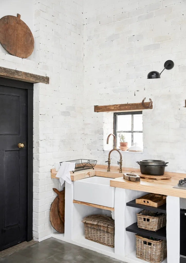 A rustic kitchen with painted white brick walls, a wooden benchtop and a small window.