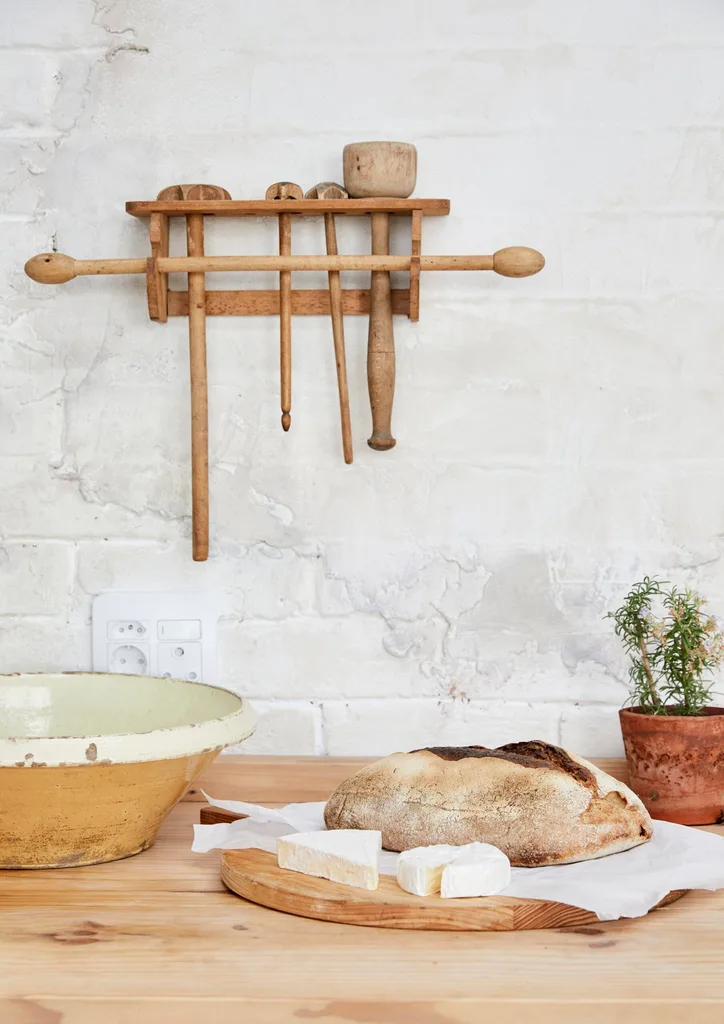 A freshly baked loaf of sourdough sits on the counter with a white brick wall in the background