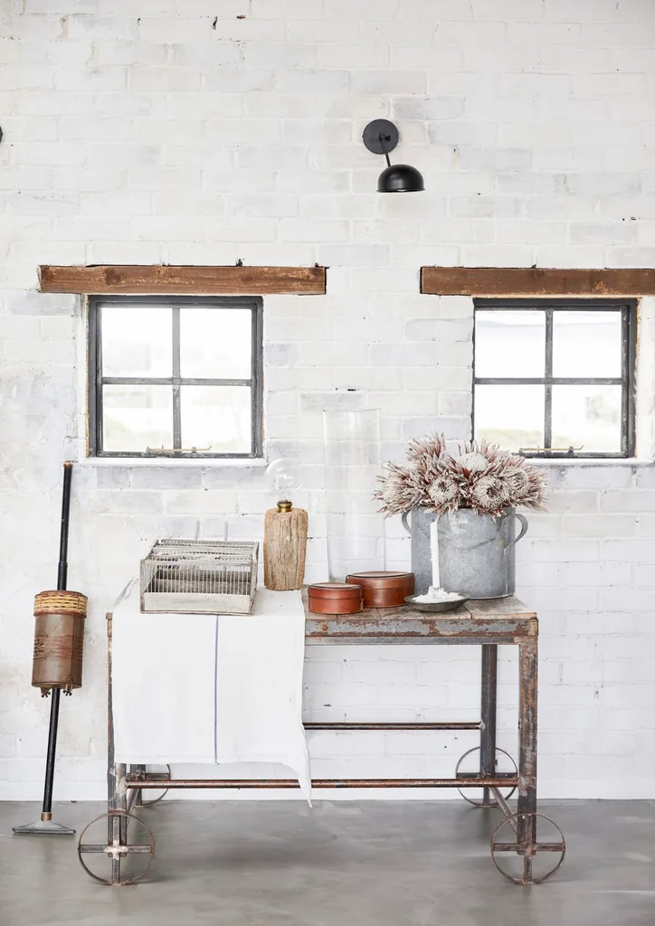 A rustic, white brick wall with two black-framed windows and antique furniture