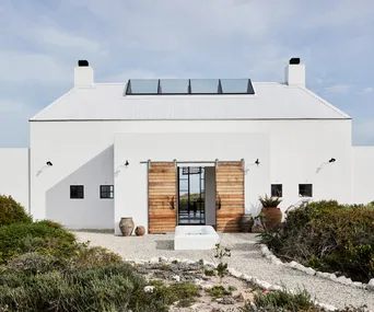 The façade of a contemporary barn-style house with white render and a large wooden barn-style front door