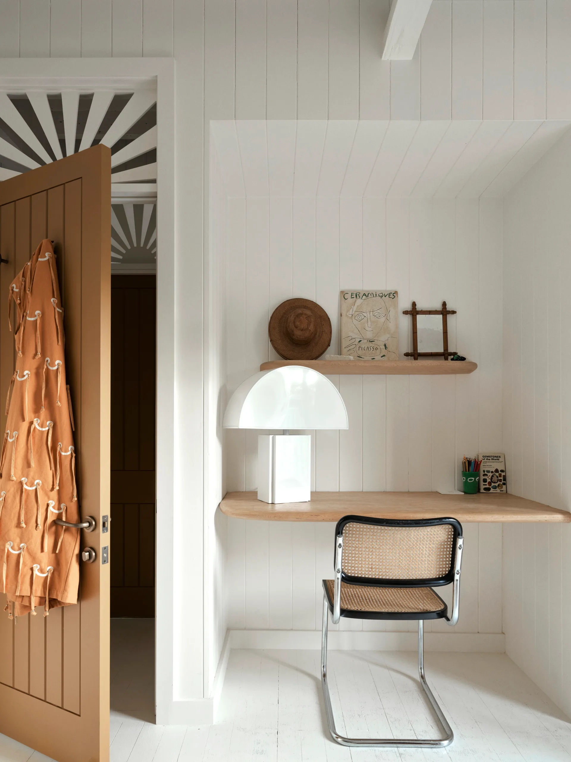 A white study rea with a rattan chair and floating shelf