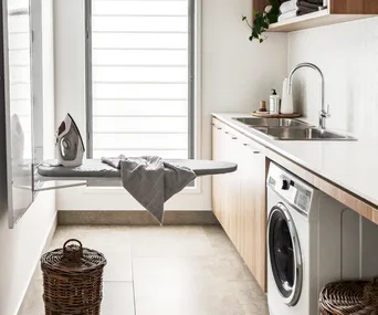 A laundry with a fold-out ironing board, a washer-dryer combo and rattan baskets