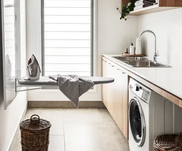 A laundry with a fold-out ironing board, a washer-dryer combo and rattan baskets