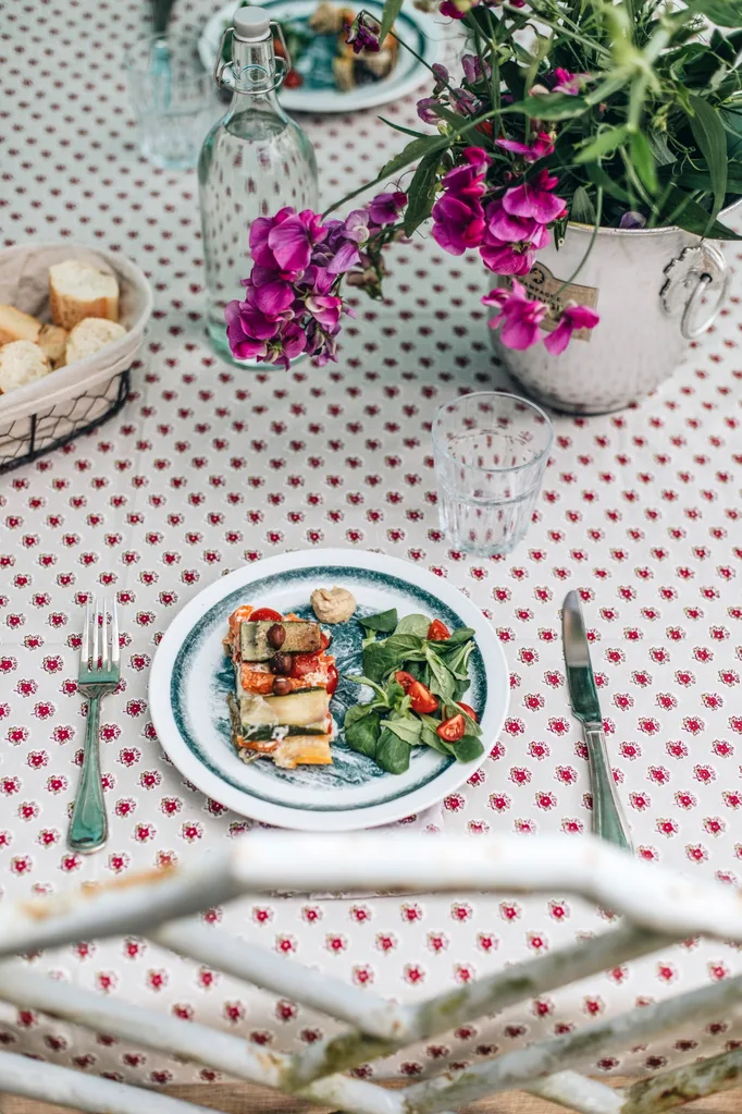 A table set for lunch, with a white and red tablecloth and a silver vase filled with flowers.