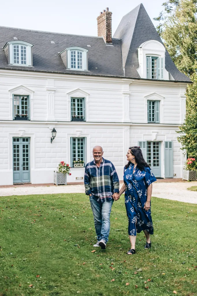 A man and a woman walk on the grass in front of a white, French-style chateau in Normandy.