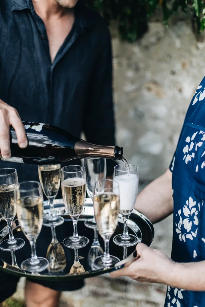 A woman holds a silver tray with champagne glasses while a man pours champagne.