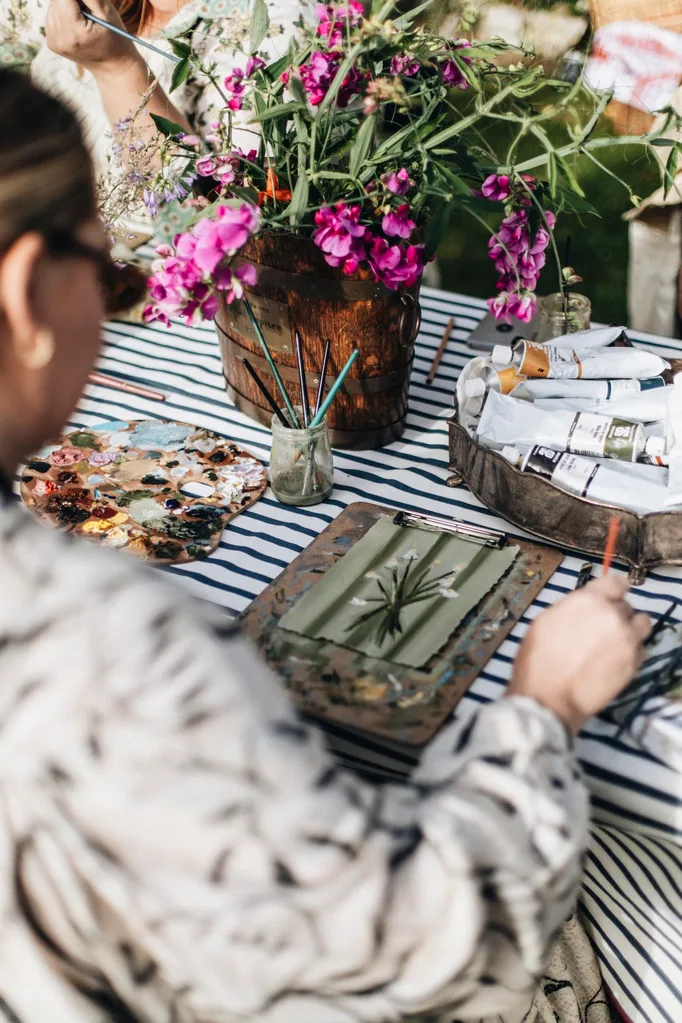 A table with a striped navy and white tablecloth covered in paint supplies and flowers.