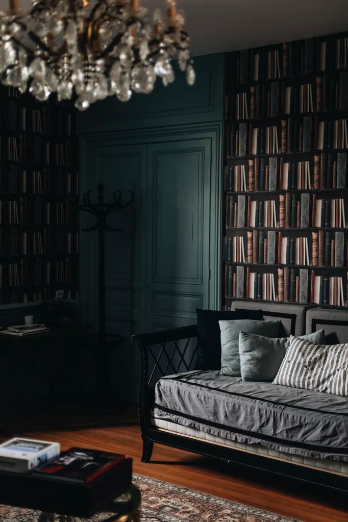 A home library is filled with antique furniture including a crystal chandelier. The double doors are painted a dark teal.