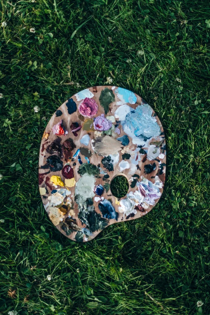 A paint-covered palette sits on lush grass.