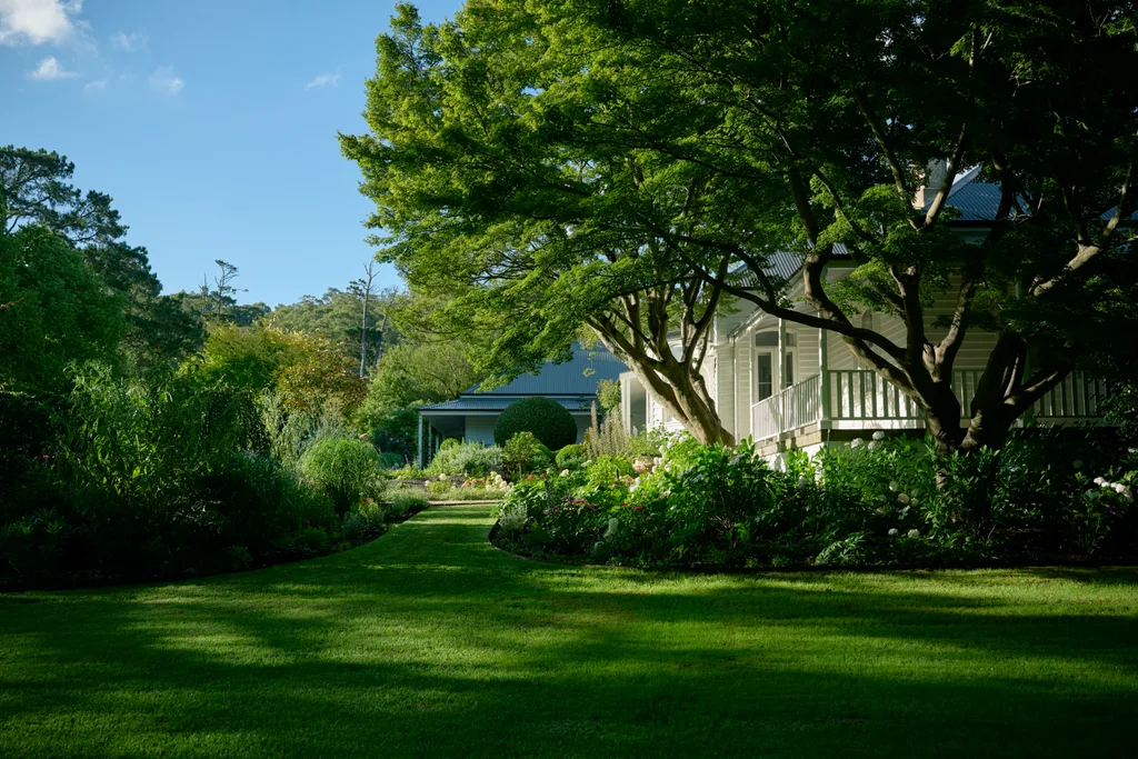 A white weatherboard home owned by Collette Dinnigan with a large green garden