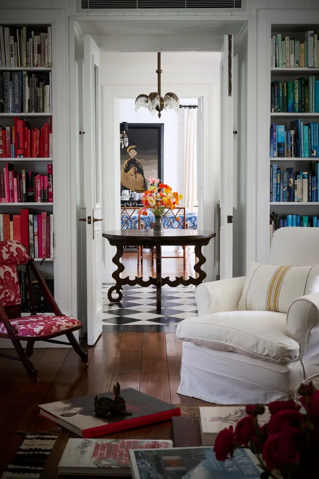 A home library with colour-coded books, a white armchair and timber coffee table