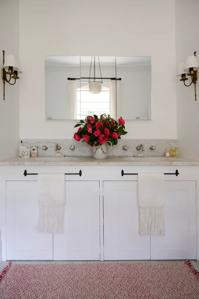 A white bathroom with wall sconces and a marble countertop