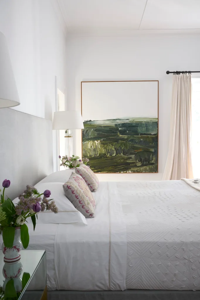 A white bedroom with white bedding and a green painting
