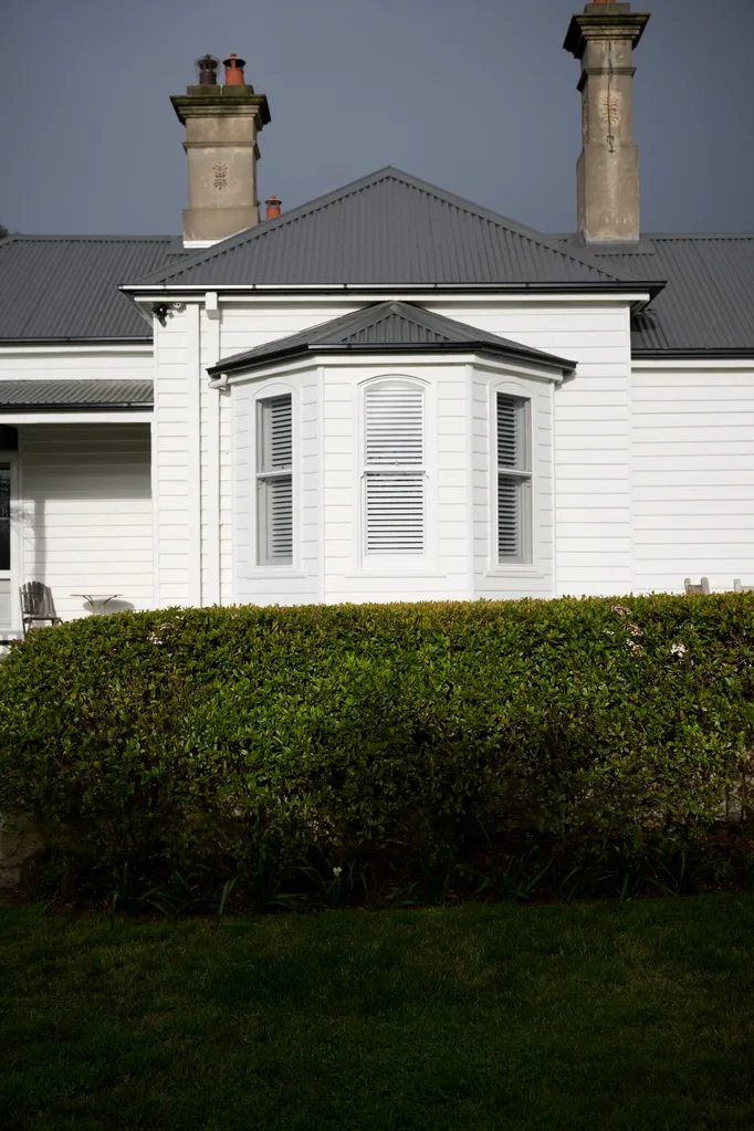A white weatherboard home surrounded by a hedge
