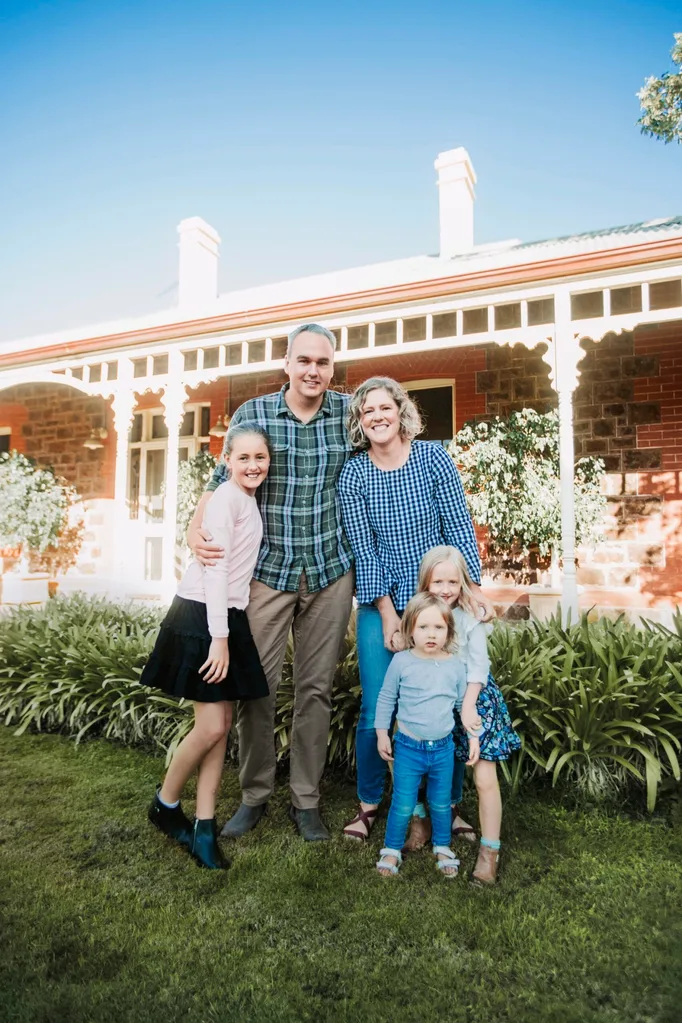 Family with three daughters outside stone house with white verandah