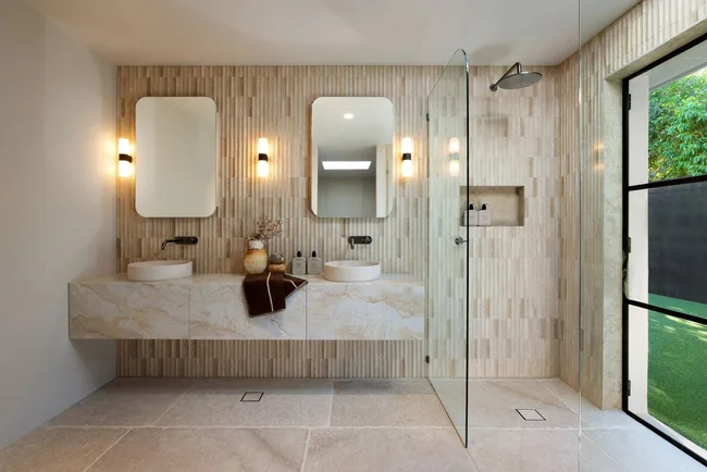 A bathroom with a double vanity, rain shower and large tiles