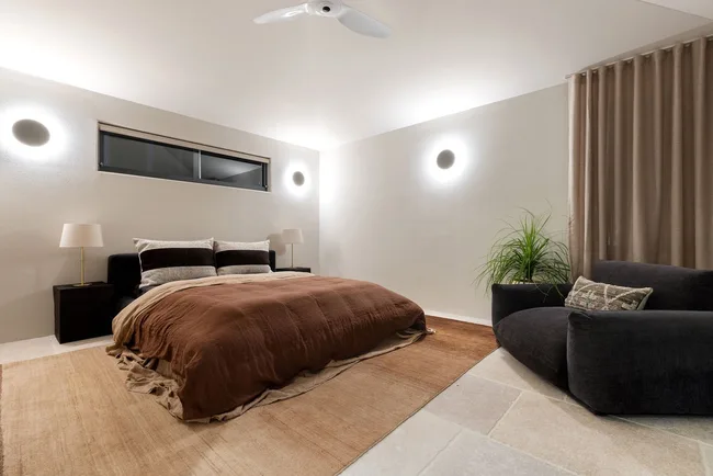 A large bedroom with neutral-toned bedding and a black armchair