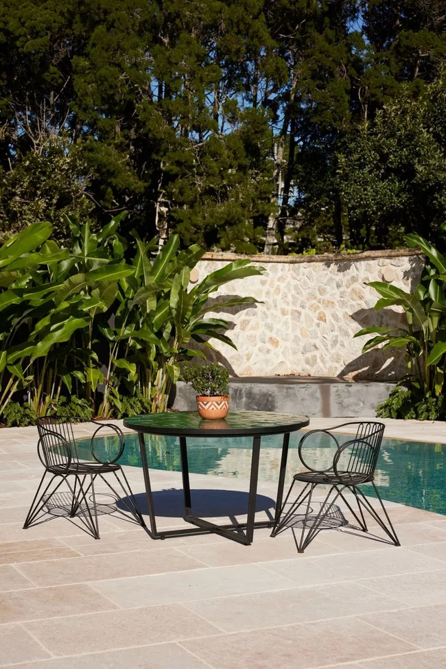 A swimming pool with tropical gardens and a three-piece outdoor dining setting