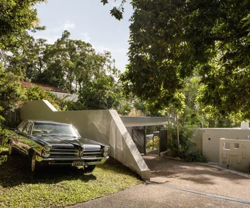 The facade of a mid-century modern home with a vintage car parked outside