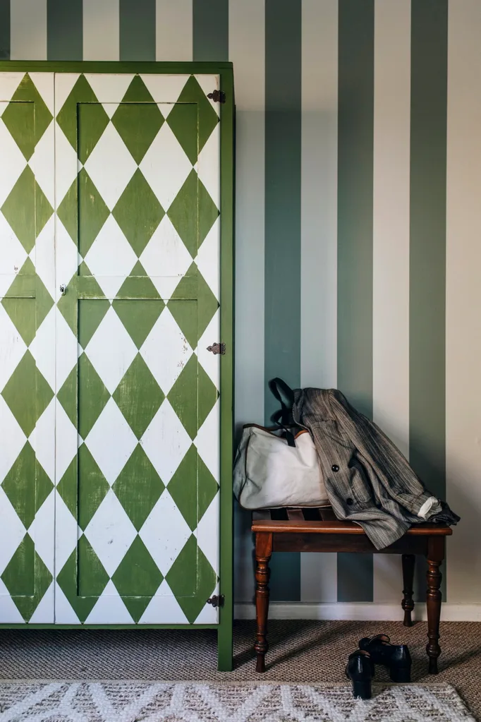 A wall with dark green and white striped wallpaper, and a green and white diamond patterned chest